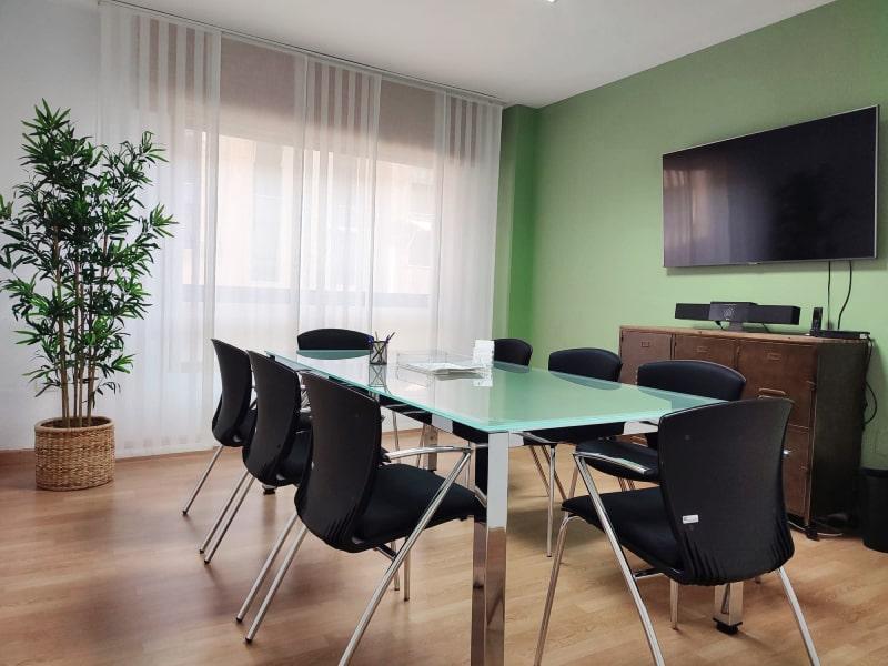 Despacho con sillas negras, mesa de cristal, pantalla de televisión y colores verdes
